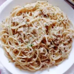 Creamy garlic canned tuna pasta on a white plate with Parmesan cheese and parsley sprinkled on top