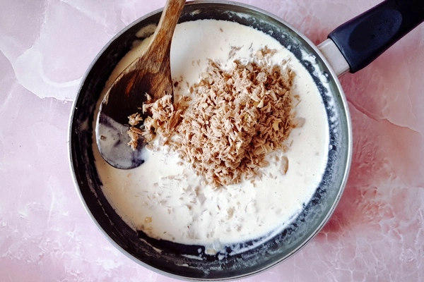 Cooked tuna added to creamy garlic sauce in a skillet with a wooden ladle