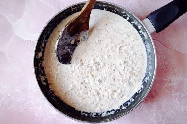 Milk added to creamy tuna sauce in a skillet with a wooden ladle