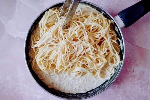 Cooked spaghetti added to creamy tuna pasta sauce in a skillet with a wooden ladle