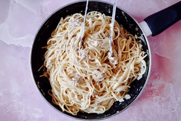 Creamy garlic canned tuna sauce mixed with cooked spaghetti in a skillet with tongs
