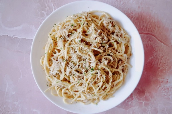 Creamy garlic canned tuna pasta on a white plate with Parmesan cheese and parsley sprinkled on top