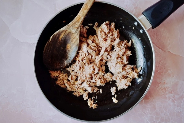 Drained canned tuna in a skillet with a wooden ladle