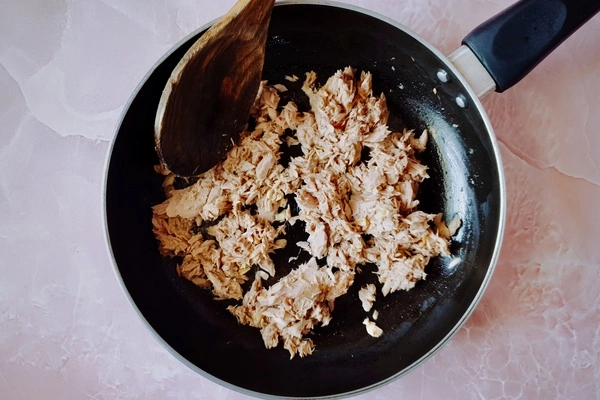 Cooked tuna in a skillet with a wooden ladle
