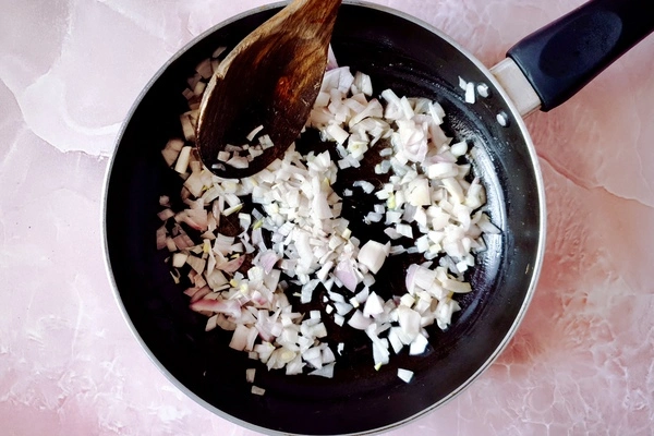 Chopped onions with butter in a skillet with a wooden ladle