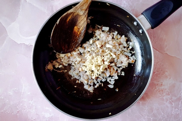 Lightly browned chopped onions with minced garlic and butter in a skillet with a wooden ladle