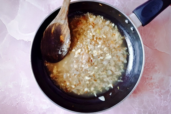 Lightly browned chopped onions with minced garlic and chicken stock in a skillet with a wooden ladle