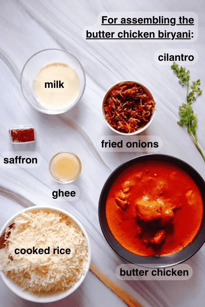 All the ingredients needed to assemble the butter chicken biryani together such as milk, saffron, fried onions, cilantro, ghee, butter chicken curry and partially cooked rice
