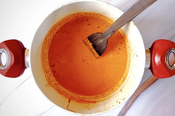 Butter chicken sauce in a Dutch oven with a wooden ladle