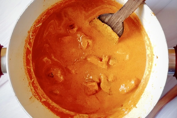 Butter chicken curry in a Dutch oven with a wooden ladle