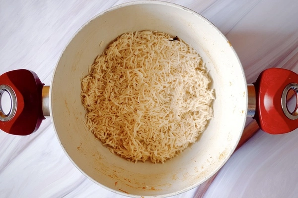 A thin layer of biryani rice spread on the bottom of a Dutch oven