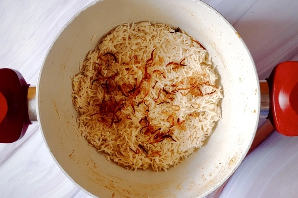Fried onions spread over biryani rice in a Dutch oven