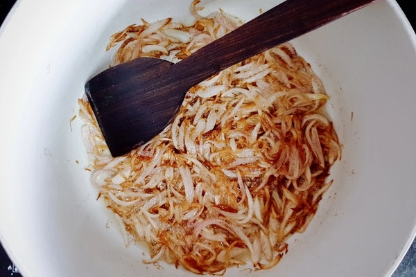 Golden brown sliced onions in a Dutch oven with a wooden ladle