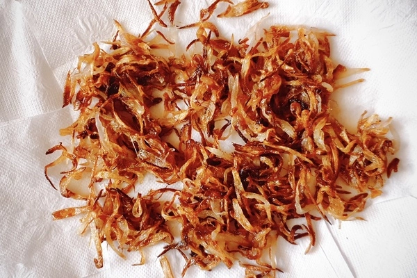 Deep golden brown sliced fried onions spread over kitchen towels