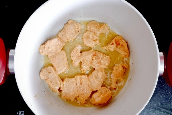 Marinated cubes of chicken cooking in butter and oil in a Dutch oven