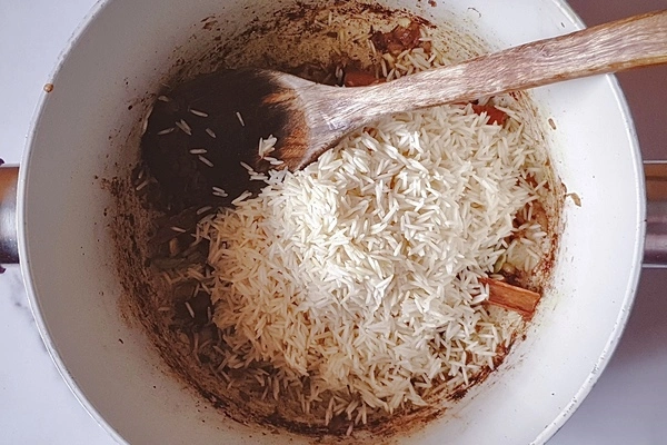 White, unboiled Basmati rice in a cooking pot with a wooden ladle