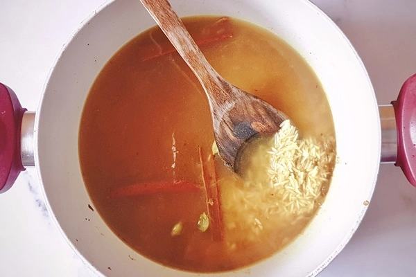 Chicken broth with uncooked toasted rice in a cooking pot