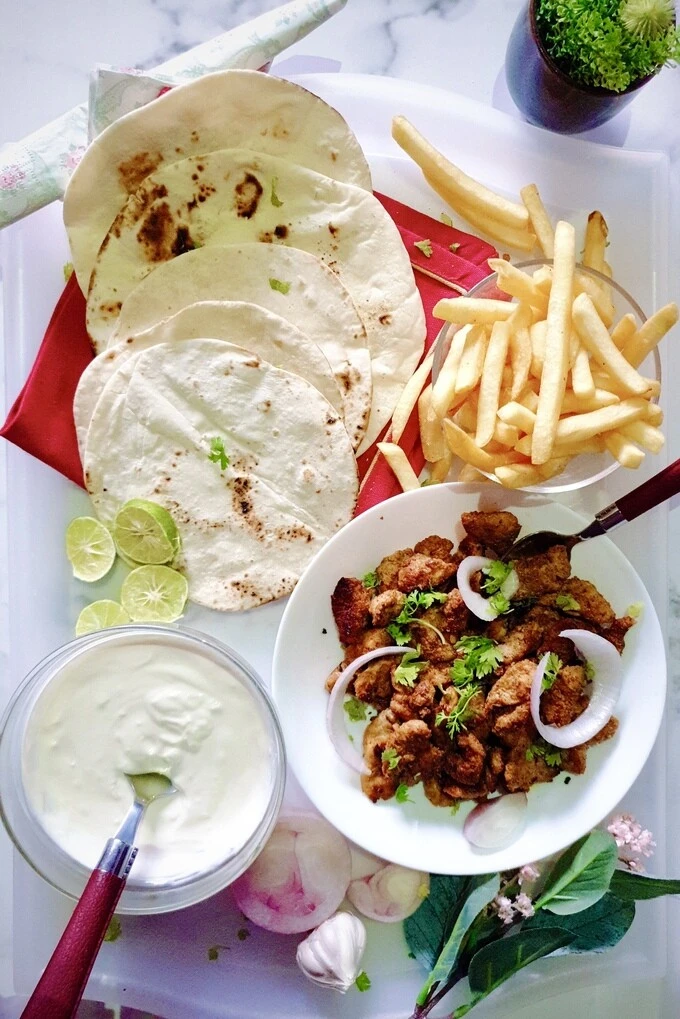 A platter of chicken shawarma chunks in a white bowl on a tray with garlic sauce, pita bread and French fries