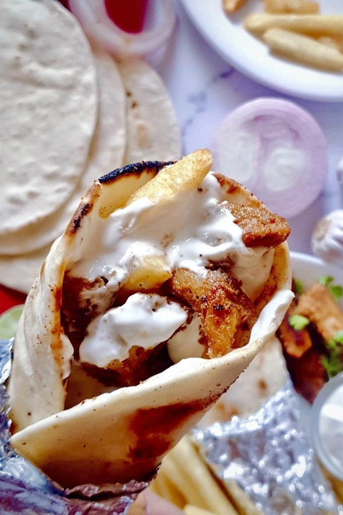 A close up of chicken shawarma wrap with creamy garlic sauce and French fries
