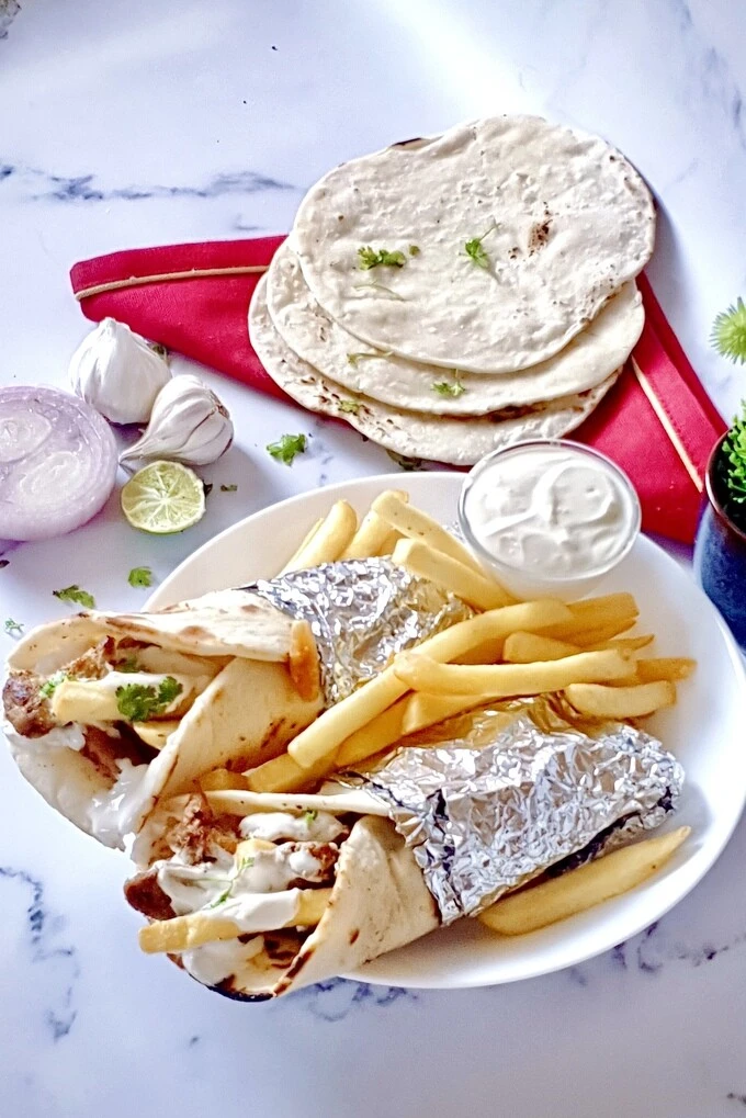 Chicken shawarma wraps with creamy garlic sauce and French fries on a white plate with pita breads on the side