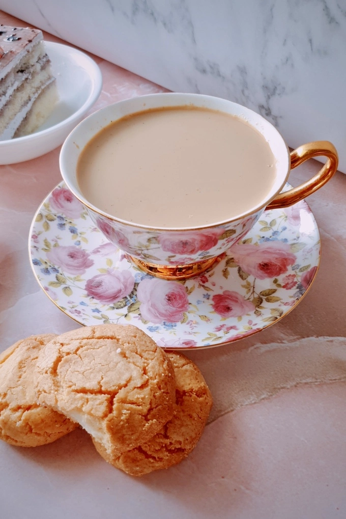 Japanese royal milk tea in a tea cup surrounded by three cookies and a slice of cake in the background