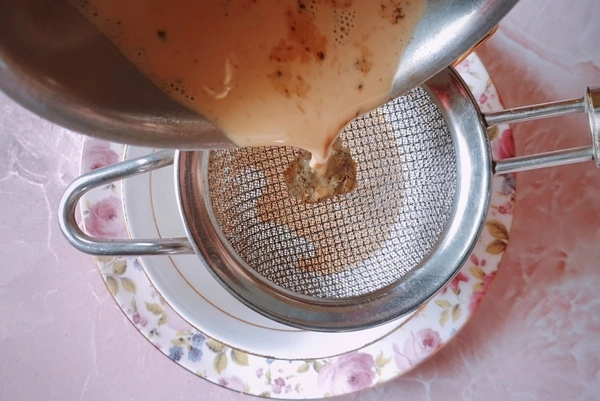 Japanese royal milk tea being poured through a fine mesh strainer into a teacup with sugar in it over a saucer