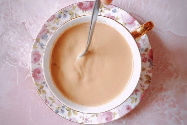 Japanese royal milk tea in a teacup over a saucer being stirred with a spoon