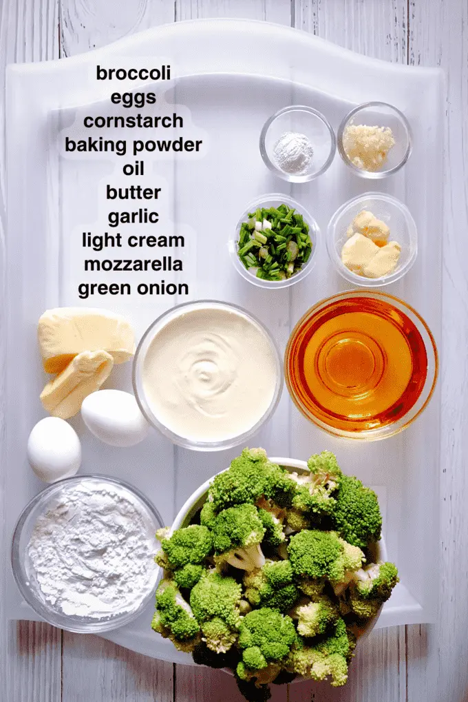 Ingredients for Homemade Batter Fried Broccoli with Creamy Sauce arranged on a platter such as broccoli florets, eggs, cornstarch. baking powder, oil, butter, garlic, light cream, mozzarella and green onion in separate bowls