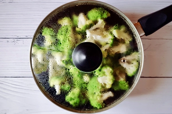 Broccoli florets steaming in a skillet covered with a lid