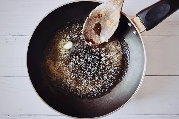 Butter being melted in a skillet with a wooden ladle