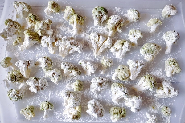 Cornstarch coated broccoli florets on a cornstarch dusted tray