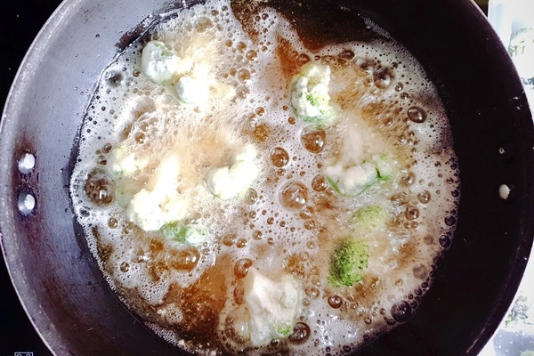 Coated broccoli florets being deep fried in a wok