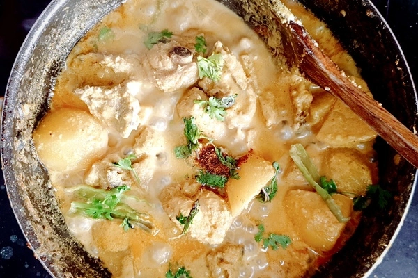 Cilantro, mint leaves, garam masala and green chili peppers added to chicken korma in a cooking pan with a wooden ladle