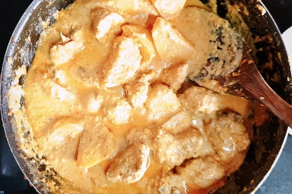 Plain yogurt and light cream mixed with chicken and potatoes curry mixture in a cooking pan with a wooden ladle