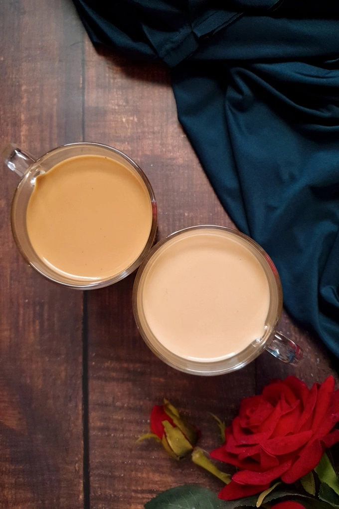 Royal milk tea and regular milk tea in glass mugs side by side with a green satin cloth and a red rose beside it