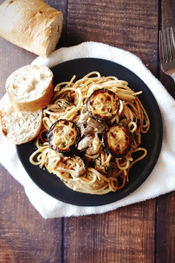 One Pot Zucchini Mushroom Pasta in a black plate placed over a white cloth with bread and bread slices and a fork on each side