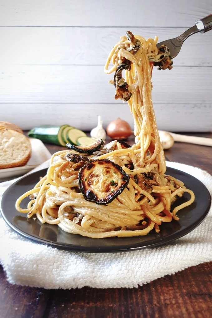 Zucchini Mushroom Pasta on a black plate placed over a white cloth with the spaghetti pasta twirled around a fork and lifted a little