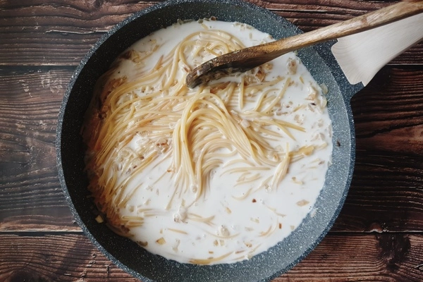 A skillet having spaghetti being mixed with coconut milk