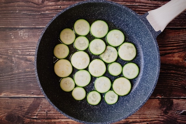 A skillet with a thin layer of oil and sliced zucchini rounds getting pan-fried in it