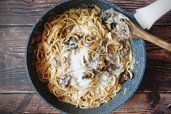 A skillet having a little coconut milk, cooked spaghetti, cooked zucchini rounds and mushrooms and a little dried parsley sprinkled in all being mixed together