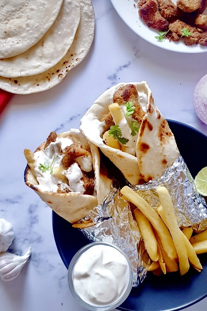 Two chicken shawarma wraps with creamy garlic sauce and French fries in a black bowl with pita breads on the side