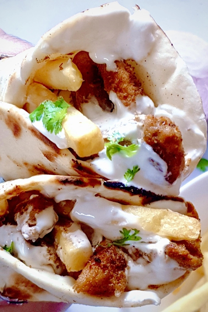 Close up of two stacked chicken shawarma wraps with creamy garlic sauce and French fries