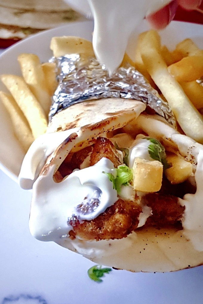 Close up of chicken shawarma wrap with creamy garlic sauce and French fries having creamy garlic sauce poured over the wrap