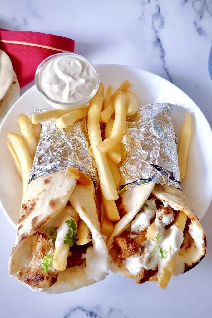 Two chicken shawarma wraps with creamy garlic sauce and French fries served on a white plate