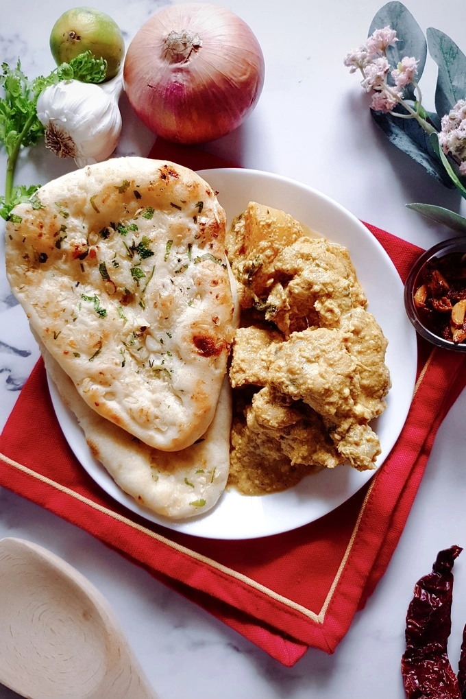 Rich and Aromatic Indian Chicken Korma Curry Cooked in Yogurt served on a white plate with two naan breads on the side everything over a red napkin
