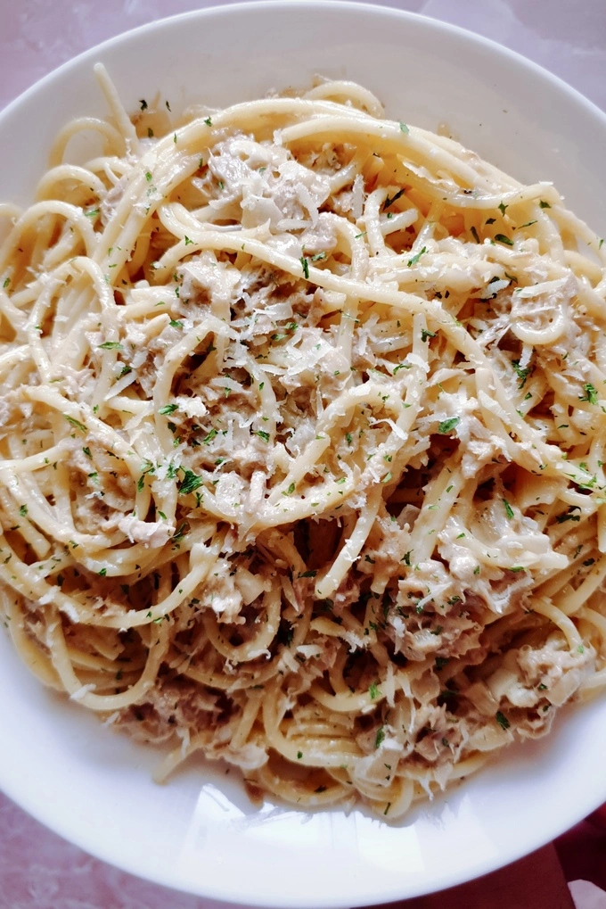 Close up of Creamy garlic canned tuna pasta recipe on a white plate with Parmesan cheese and parsley sprinkled on top