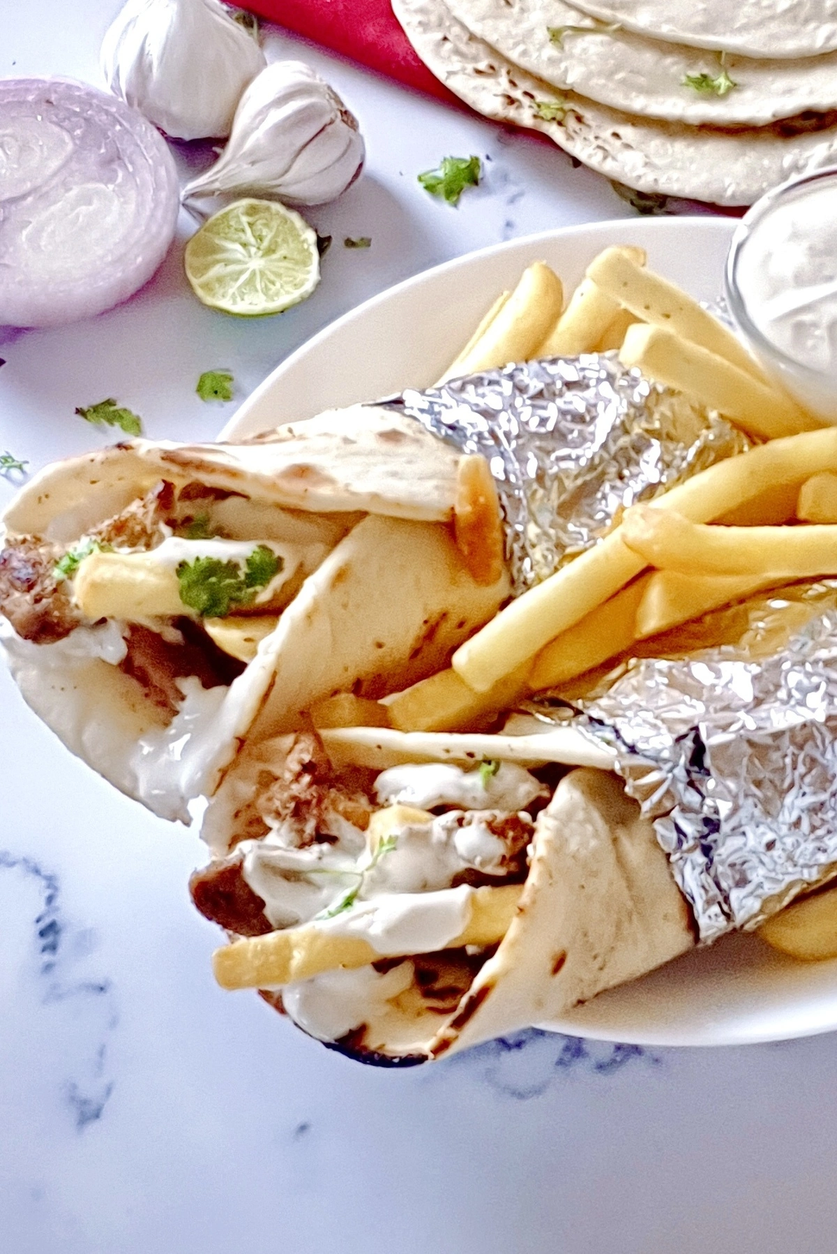 Two easy chicken shawarma wraps with creamy garlic sauce and French fries on a white plate