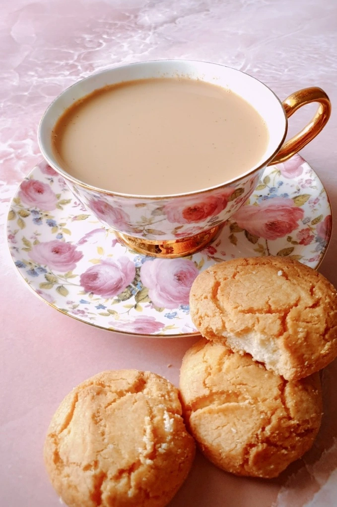 Homemade Japanese Royal Milk Tea in a fancy teacup over a plate and three cookies in front with one cookie bitten into