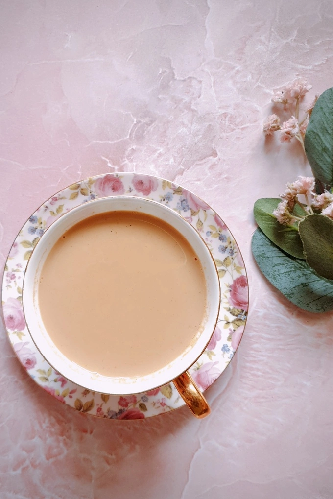 Top view of Homemade Japanese Royal Milk Tea in a fancy teacup over a plate on the left and a flower for decor on the right