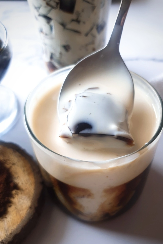 Close up of Homemade Coffee Jello Recipe with Condensed Milk Cream in a small glass with a spoon inserted in it and removed with a bite size piece of coffee jelly